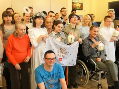 Mieszkańcy i uczniowie w strojach aniołów z transparentem „Po kolędzie”