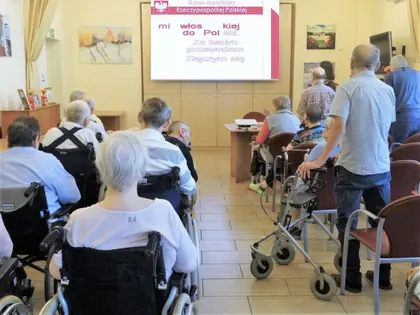 Mieszkańcy śpiewają hymn przed ekranem z tekstem w świetlicy