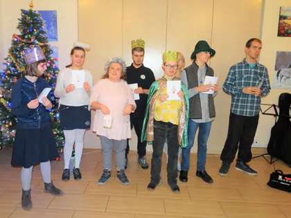 Kolędnicy w koronach i kapeluszach śpiewają przy choince