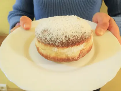 Pączek posypany cukrem pudrem na białym talerzu trzymanym w dłoniach