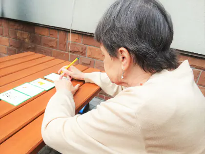 Mieszkanka rozwiązuje zadanie z kartami przy stole w ogrodzie