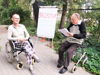 Mieszkanka na wózku i mieszkaniec czytają tekst przy tablicy z napisem Balladyna