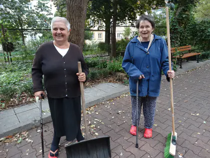 Uśmiechnięte mieszkanki z łopatą i miotłą sprzątają podwórko