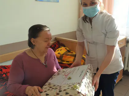 Opiekunka w maseczce i czapce Mikołaja wręcza prezent mieszkance