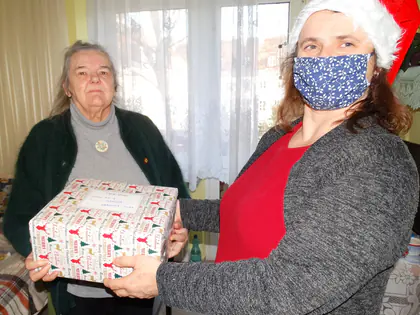 Opiekunka w maseczce wręcza mieszkance świąteczną paczkę