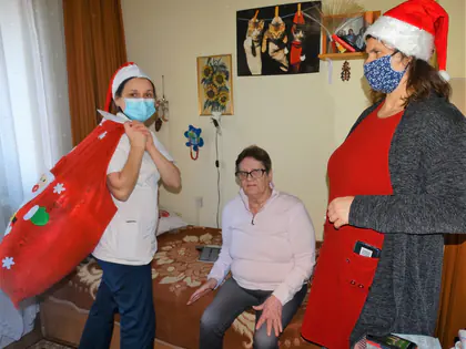Opiekunki w czapkach Mikołaja z workiem prezentów w pokoju mieszkanki