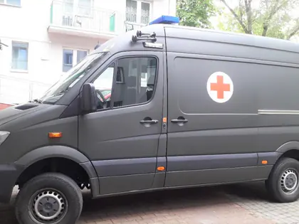 Wojskowy ambulans z czerwonym krzyżem zaparkowany przed budynkiem Domu