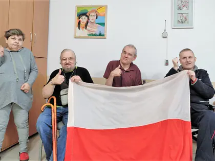 Mieszkańcy trzymają biało-czerwoną flagę i unoszą kciuki
