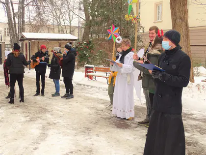 Młodzież w strojach kolędników występuje na zaśnieżonym podwórku Domu