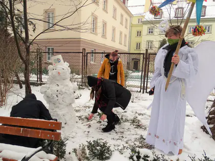 Anioł z gwiazdą i kolędnicy lepią bałwana w ogrodzie