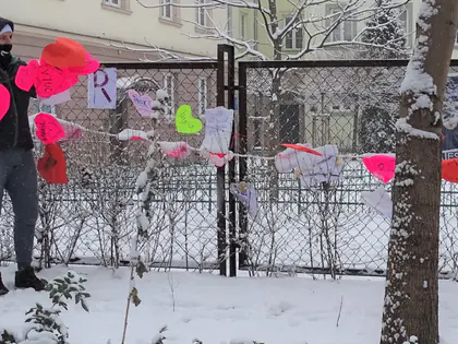 Kolorowe walentynkowe serca na siatce ogrodzenia, obok młodzież w kurtkach