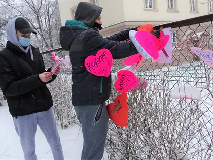 Młodzież w maseczkach wiesza papierowe serca na ogrodzeniu w zimie