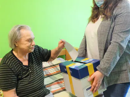 Kobieta w maseczce trzyma urnę, mieszkaniec wrzuca kartę