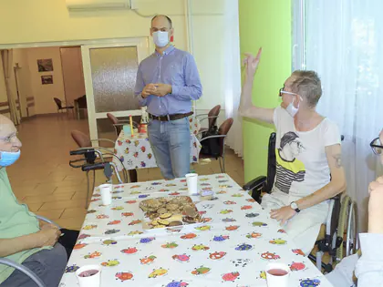 Mieszkańcy siedzą przy stole w kolorową łąkę, prowadzący stoi