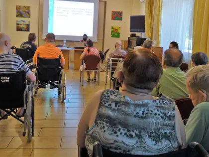 Mieszkańcy słuchają prelekcji wyświetlanej na ekranie