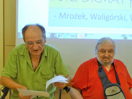 Dwaj mieszkańcy czytają role z kartek przed ekranem