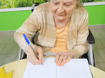 Starsza mieszkanka pisze w zeszycie przy stole z jarzębiną