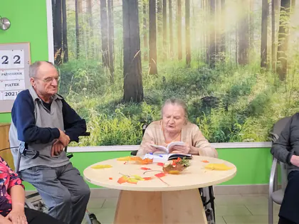 Mieszkańcy siedzą przy okrągłym stole na tle fototapety z lasem