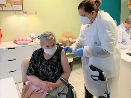 Mieszkanka z balkonikiem otrzymuje szczepienie od pracownicy przychodni w fartuchu ochronnym