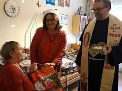 Kobieta i zakonnik wręczają mieszkance świąteczną torbę z prezentami