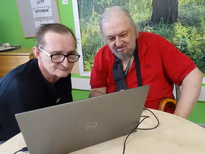 Dwaj mieszkańcy pracują razem przy laptopie podczas warsztatów komputerowych