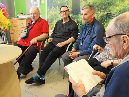 Mieszkańcy czytają wiersze przy okrągłym stoliku z kwiatami