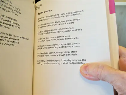 Dłoń trzyma otwartą książkę z wierszem Śpiew słowika