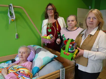 Pracownice wręczają koszyczek wielkanocny mieszkance leżącej w łóżku