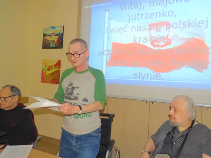 Mieszkaniec śpiewa z kartki przed ekranem z tekstem pieśni