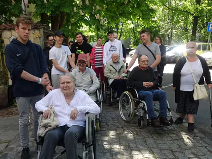 Mieszkańcy na wózkach i młodzież na podwórku przy kwitnących kasztanowcach