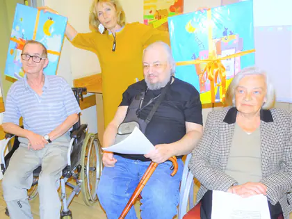 Trzech mieszkańców pozuje z kobietą trzymającą kolorowe obrazy