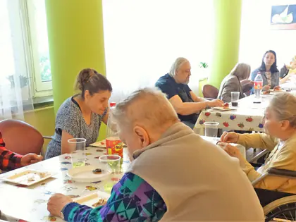 Mieszkańcy i goście przy stołach z poczęstunkiem w świetlicy