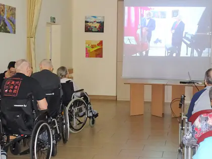 Mieszkańcy na wózkach przed ekranem z nagraniem koncertu