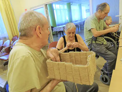 Mieszkańcy oplatają sznurkiem pudełko z recyklingu podczas warsztatów rękodzieła