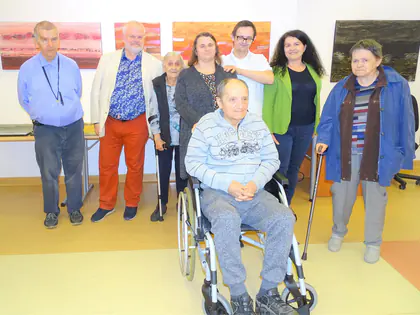 Mieszkańcy, jeden na wózku, pozują w galerii z obrazami