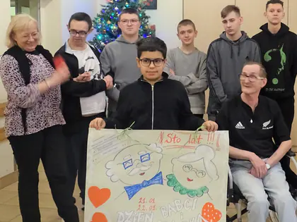 Młodzież i mieszkańcy trzymają plakat z napisem Sto lat, Dzień Babci i Dziadka