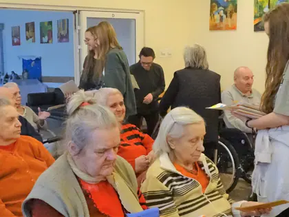 Młoda kobieta rozdaje kartki mieszkankom siedzącym w świetlicy