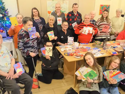 Licealistki i mieszkańcy pozują z kolorowymi kartkami i upominkami przy choince