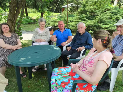 Mieszkańcy siedzą przy okrągłym stoliku w ogrodzie podczas pikniku
