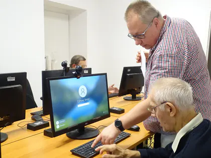 Prowadzący pomaga seniorowi przy klawiaturze komputera