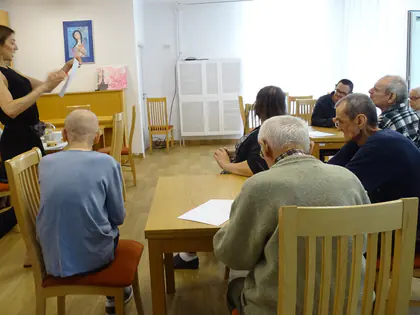 Prowadząca śpiewa z mieszkańcami siedzącymi przy stołach