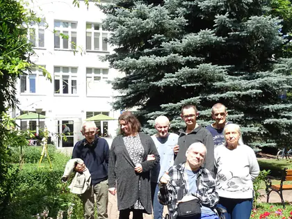Mieszkańcy i opiekunowie pozują w ogrodzie przy świerku