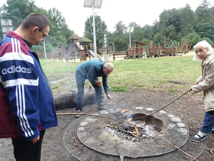 Mieszkańcy pieką kiełbaski nad ogniskiem w parku