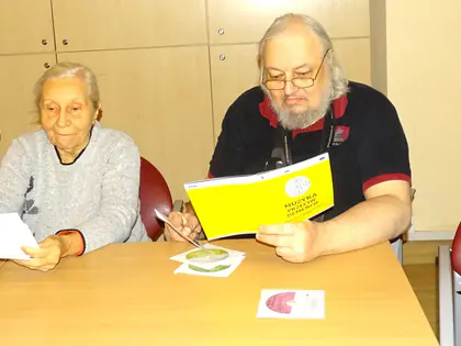 Mieszkańcy śpiewają z kartek przy stole