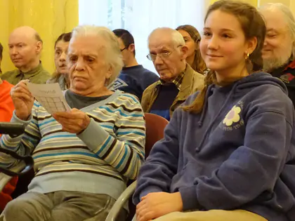 Mieszkańcy i dziewczyna śpiewają z kartek siedząc obok siebie