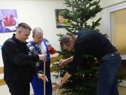 Mężczyźni stawiają choinkę w stojaku w świetlicy