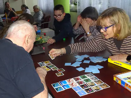 Mieszkańcy i kobieta w okularach układają karty do gry w memory