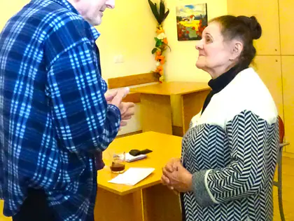 Starszy mężczyzna w kratkowanej koszuli rozmawia z kobietą w żakiecie w sali