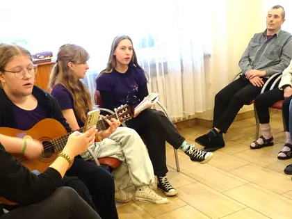 Harcerki grają na gitarach i śpiewają dla mieszkańców siedzących obok
