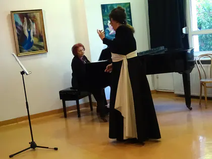 Śpiewaczka w czarnej sukni występuje obok pianistki przy fortepianie